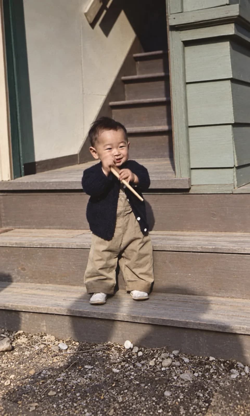 Restored: toddler in a dark cardigan holding a stick on wooden porch steps