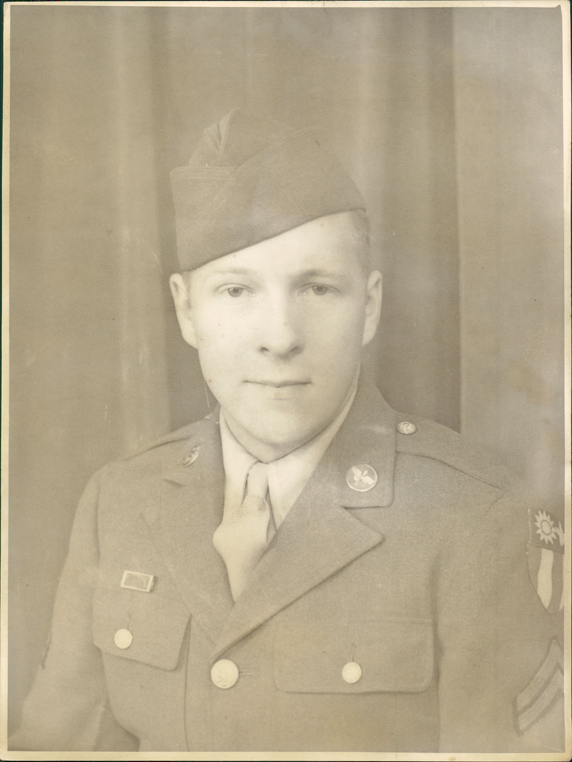 Creased and yellowed photograph of a young soldier in uniform before restoration.