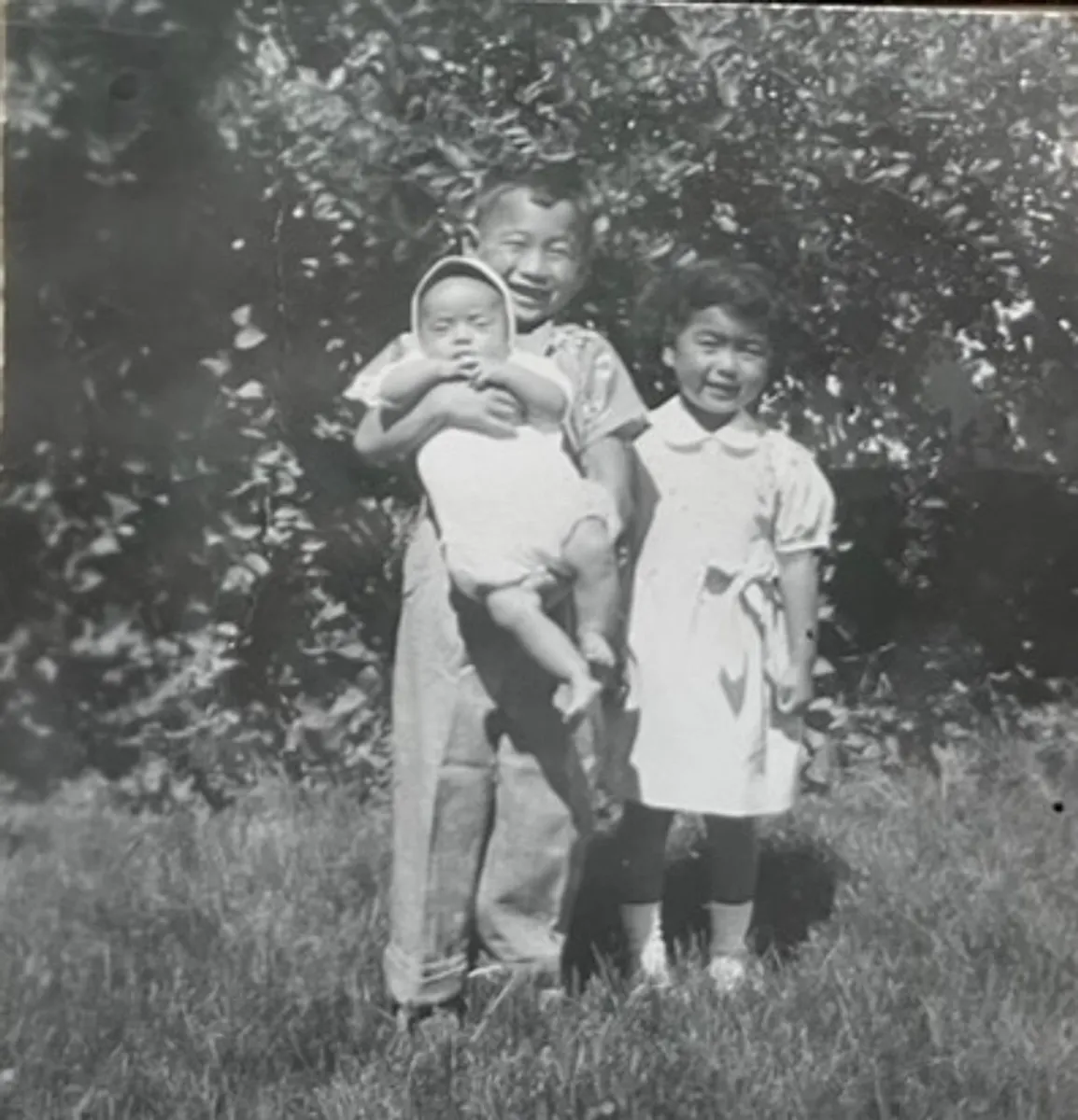 Before: black-and-white snapshot of a boy holding a baby next to a young girl on a lawn