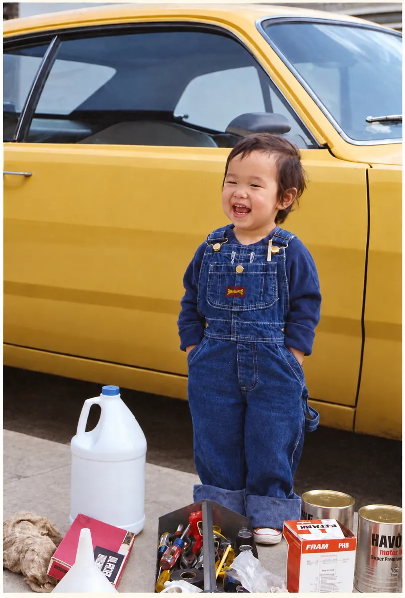 After: faded snapshot of a toddler in overalls standing beside a yellow car